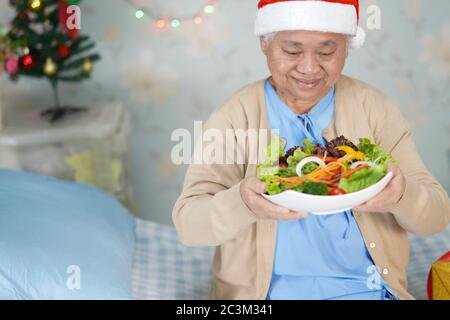 Asiatische ältere oder ältere alte Dame Frau Patient mit Santa Claus Helferhut mit Salat Gemüse gesunde Lebensmittel in weihnachten und Neujahr Feier Stockfoto