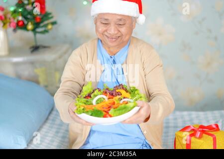 Asiatische ältere oder ältere alte Dame Frau Patient mit Santa Claus Helferhut mit Salat Gemüse gesunde Lebensmittel in weihnachten und Neujahr Feier Stockfoto