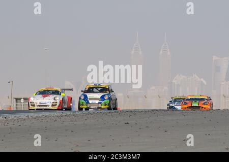 DUBAI - JANUAR 14: Porsche 997, BMW Mini und Ginetta G50 mit Dubai City im Hintergrund, während des 2012 Dunlop 24 Stunden Rennens auf dem Dubai Autodrome on Stockfoto