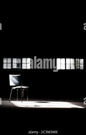 Vertikale Aufnahme eines leeren Stuhls im dunklen Raum Mit einem kleinen Licht aus dem Fenster Stockfoto