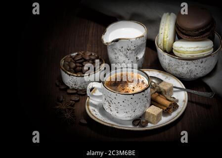 Vintage Stillleben mit Tasse Kaffee, Makronen, Kaffeebohnen, Sahne und Leinenservietten sind auf dunklem Hintergrund, mit Copy-Space Stockfoto