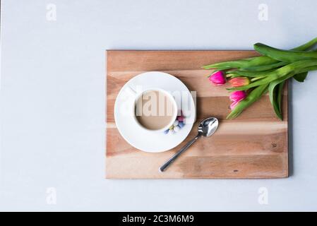 Schöne Aufnahme einer Tasse Kaffee serviert auf einem Holztablett mit Löffel und Tulpen daneben Stockfoto