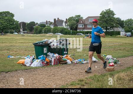 WIMBLEDON LONDON, GROSSBRITANNIEN. 21. Juni 2020. Ein Jogger läuft an Mülltonnen vorbei, die mit Müll überfüllt sind, darunter leere Pizzabäckchen, Bierflaschen, Dosen und Plastiktüten auf Wimbledon Common, nachdem die Regierung die Sperrbeschränkungen lockerte und Menschen erlaubte, sich in Gruppen von bis zu sechs Personen im Freien zu versammeln. Kredit: amer ghazzal/Alamy Live Nachrichten Stockfoto