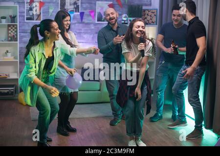 Glückliche Frau singt für ihre Freunde auf der Party. Karaoke-Unterhaltung. Stockfoto