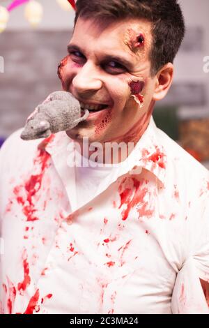 Mann verkleidet wie ein blutiger Zombie mit einer Ratte im Mund bei halloween Feier. Stockfoto