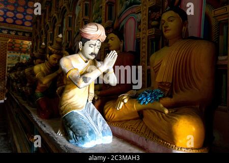 Ein Sonnenstrahl leuchtet eine menschliche Figur, die eine sitzende Buddha-Statue im Image House in Wewurukannala Vihara in Dickwella in Sri Lanka anbetet. Stockfoto