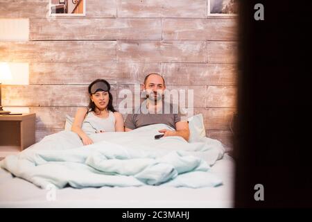 Kaukasische Ehepaar im Pyjama Fernsehen auf gemütlichen Bett liegen. Stockfoto