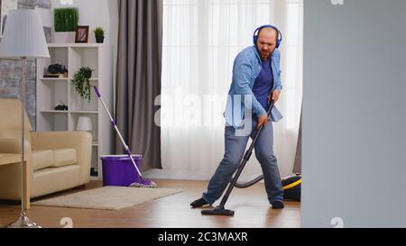 Lustiger junger Mann, der Musik auf Kopfhörern hört, während er den Boden mit Staubsauger reinigt. Stockfoto