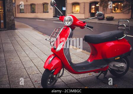 Roter Retro-Roller, altmodisches Motorrad, wird auf dem Straßensteig in der Stadt geparkt. Stockfoto