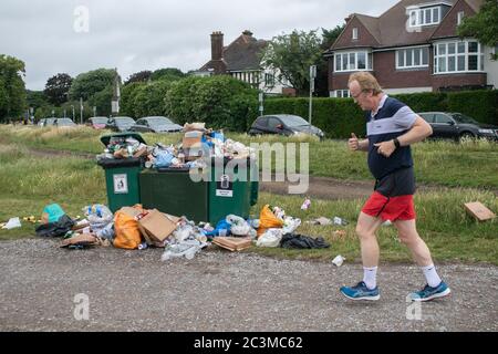 WIMBLEDON LONDON, GROSSBRITANNIEN. 21. Juni 2020. Ein Jogger läuft an Mülltonnen vorbei, die mit Müll überfüllt sind, darunter leere Pizzabäckchen, Bierflaschen, Dosen und Plastiktüten auf Wimbledon Common, nachdem die Regierung die Sperrbeschränkungen lockerte und Menschen erlaubte, sich in Gruppen von bis zu sechs Personen im Freien zu versammeln. Kredit: amer ghazzal/Alamy Live Nachrichten Stockfoto