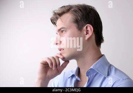 Junger Mann mit einem blauen Hemd, der tiefe Gedanken im Stehen hat Gegen eine weiße Wand Stockfoto