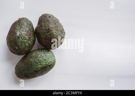 High-Angle-Aufnahme von drei reifen Avocados unter den Lichtern Isoliert auf grauem Hintergrund Stockfoto