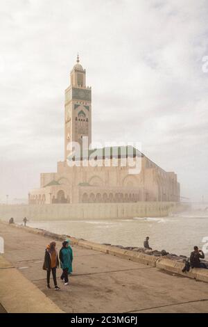 Eine Gruppe von Menschen, die während eines nebligen Nachmittags um die Moschee Hassan II. In Casablanca, Marokko, herum gehen und den Blick auf das Meer genießen Stockfoto