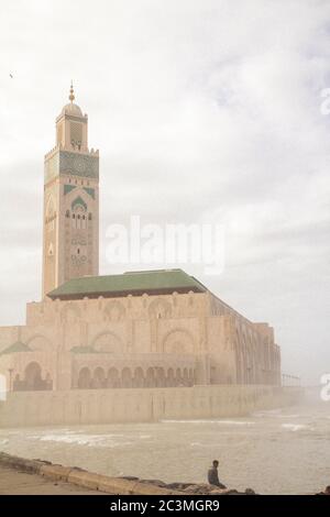 Eine Gruppe von Menschen, die während eines nebligen Nachmittags um die Moschee Hassan II. In Casablanca, Marokko, herum gehen und den Blick auf das Meer genießen Stockfoto