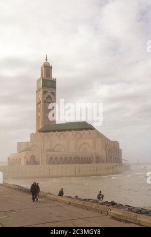 Eine Gruppe von Menschen, die während eines nebligen Nachmittags um die Moschee Hassan II. In Casablanca, Marokko, herum gehen und den Blick auf das Meer genießen Stockfoto