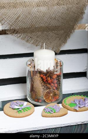 Lebkuchen Kekse mit Glasur verziert. Auf einigen Bändern, die an einer Schleife gebunden sind. In der Nähe ist eine Kerze in einem Kerzenständer. Auf weiß lackierten Brettern liegen. Stockfoto