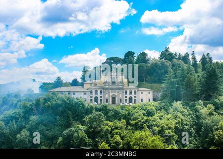 Caprarola, Viterbo, Latium, Italien - die Fassade der Kirche von Santa Teresa, umgeben von Bäumen und Grün. Blauer Himmel mit weißen Wolken. Stockfoto