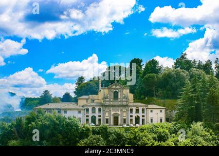 Caprarola, Viterbo, Latium, Italien - die Fassade der Kirche von Santa Teresa, umgeben von Bäumen und Grün. Blauer Himmel mit weißen Wolken. Stockfoto