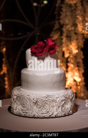 Dreistufiger Kuchen mit Hochzeit mit Buttercreme-Rosen auf der Basis, gekrönt mit roten Rosen Stockfoto