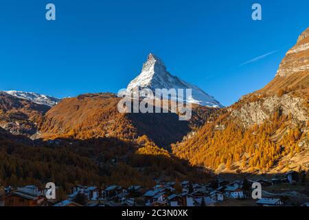 Atemberaubende Luftpanoramasicht der Stadt Zermatt mit dem berühmten Matterhorn Gipfel der Schweizer Alpen im Hintergrund und goldenem Wald am sonnigen Herbsttag mit b Stockfoto