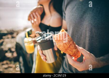 Sie hielten für einen Snack. Nahaufnahme. Croissants, Thermobecher mit Kaffee oder Tee und Saft. Picknick am Wasser. Glückliche Familie auf einem Roadtrip Stockfoto