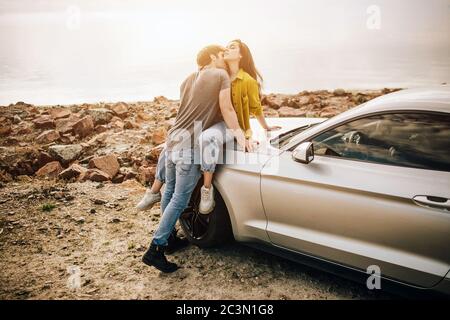 Romantisches junges Paar, das einen besonderen Moment im Freien teilt. Junges Paar verliebt auf einem Road Trip. Paar umarmen einander während sitzen auf Kapuze Stockfoto