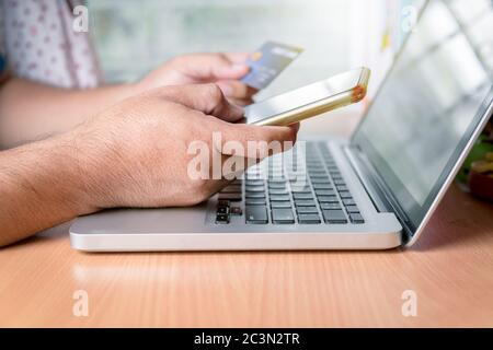Hand Mann hält Smartphone und hält Kreditkarte auf Laptop, Online-Shopping und neue normale Konzept Stockfoto