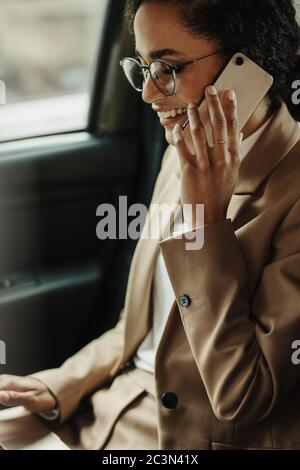 Weibliche Führungskraft, die mit ihrem Laptop arbeitet und mit ihrem Handy telefoniert, während sie mit ihrem Auto unterwegs ist. Geschäftsfrau sitzt auf dem Rücksitz des Autos mit Laptop und p Stockfoto