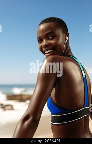 Afrikanische Frau in Sportbekleidung, die eine Pause nach dem Training im Freien. Fitness Frau trägt Musik hören auf Kopfhörer und lächelt. Stockfoto