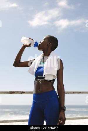 Fit Frau Trinkwasser nach dem Training. Durstige Sportlerin trinkt Wasser im Freien auf der Straße am Meer. Stockfoto