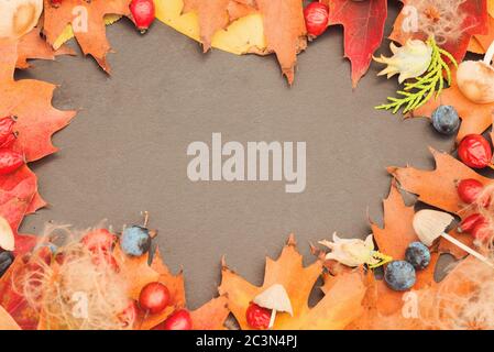 Herbsthintergrund mit schönen Blättern, Hagebutten, Walnüssen, Waldpilzen auf einem alten dunklen Tisch. Mockup für saisonale Angebote und eine Urlaubskarte. Stockfoto