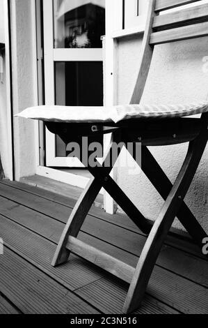 Vertikale Graustufenaufnahme eines hölzernen Stuhls gegen das Fenster In einem Balkon Stockfoto