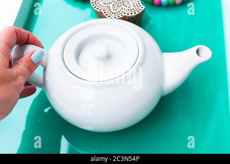 Nahaufnahme einer weiblichen Hand, aus der eine Teekanne greift Ein türkisfarbenes Tablett Stockfoto