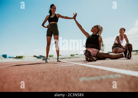 Frauen Athleten, die eine Pause nach dem Training sitzen auf der Laufstrecke und geben High Five im Stadion. Gruppe von drei Sprintern entspannen auf rac Stockfoto