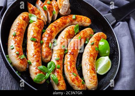 Langes Frühstück Wurst Links von Schweinefleisch auf einer Pfanne, serviert mit frischem Basilikum und Frühlingszwiebeln, Limettenkeile, auf einem dunklen Holzhintergrund, Top vie Stockfoto