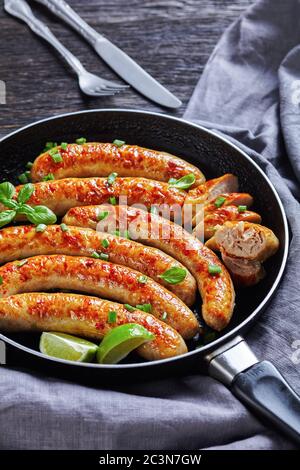 Gebratene Schweinewurst Links von Hackfleisch auf einer Pfanne, serviert mit frischem Basilikum und Frühlingszwiebeln, Kalk Keile, auf einem dunklen Holztisch mit Besteck, V Stockfoto