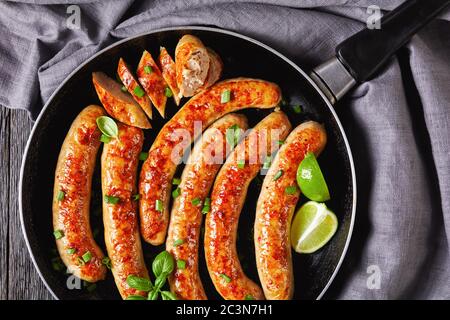 Frühstück Schweinefleisch Wurstlinks oder Patties auf einer Pfanne mit frischem Basilikum und Frühlingszwiebeln auf einem dunklen Holzhintergrund mit Besteck, Kalk verpaßt gebraten Stockfoto