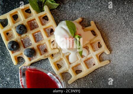 Frisch gebackene hausgemachte klassische belgische Waffeln mit Eiscreme, frischen Blaubeeren und Minze, Blick von oben. Herzhafte Waffeln. Frühstückskonzept. Stockfoto