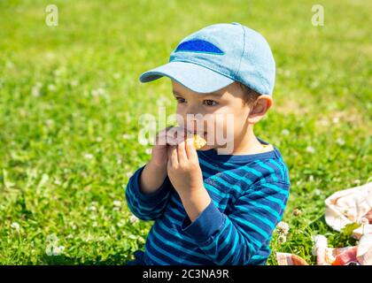 Kleiner Junge, der auf dem Rasen Keks isst Stockfoto