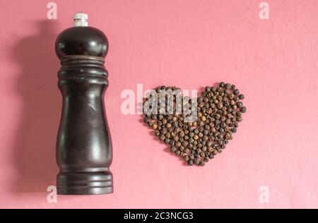 Herzförmiger schwarzer Pfeffer Schwarze Pfefferkörner in Form eines Herzens auf dem rosa Holztisch.valentinstag-Konzept. Stockfoto