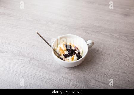 Vanilleeis mit Brombeermarmelade in einer weißen Tasse auf hellem Holzhintergrund Stockfoto