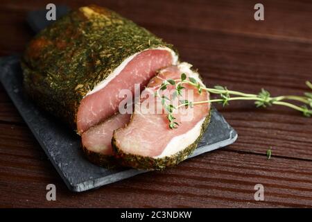 Getrocknetes Schweinefleisch, Polendwitz, ruckiges Filet, frischer grüner Thymian, Schieferschneidebrett auf Holzhintergrund. Schweinehälte. Poleniza ist ein trocken ausgehärtetes Filet Stockfoto