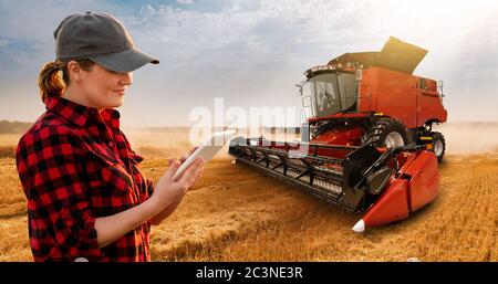 Frau Farmer mit digitalem Tablet auf einem Hintergrund von Harvester. Smart Farming-Konzept. Stockfoto