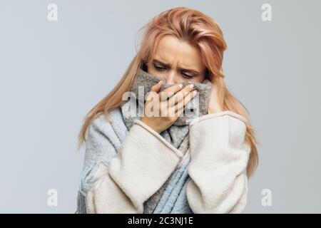 Verärgert junge kaukasische Frau mit Erdbeer blonden Haaren in warmen Schal gewickelt, fühlt sich schlecht, Blick auf Kamera, closeup.Sick verzweifelt Frau hat Grippe. Rh Stockfoto