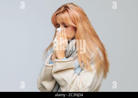 Nette kranke junge Frau mit Erdbeer blonden Haaren niesen oder mit handkerchieif, um den Nieselkopf von ihrer Nase zu wischen. Rhinitis, Erkältung, Krankheit, Allergie-Koncep Stockfoto