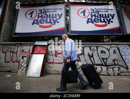 Der Mann mit dem Koffer kommt vor einer Kampagne an den Plakatwänden der regierenden Serbischen Fortschrittspartei (SNS) des amtierenden Präsidenten Aleksandar Vucic vorbei Stockfoto