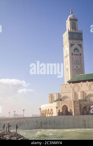 Eine Gruppe von Männern, die im Meer vor der Moschee Hassan II in Casablanca, Marokko, an einem Nachmittag im Herbst fischen Stockfoto