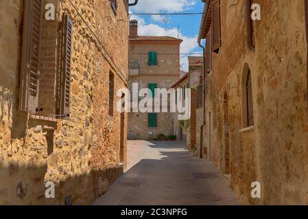 Schöne schmale Straße mit Sonnenlicht und Blumen in der kleinen magischen und alten Dorf Pienza, Val D'Orcia Toskana, Italien Stockfoto