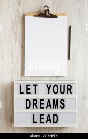 'Lass deine Träume führen' auf einem Leuchtkasten, Zwischenablage mit leerem Blatt Papier auf einer weißen Holzfläche, Draufsicht. Flach, über Kopf, von oben. Stockfoto
