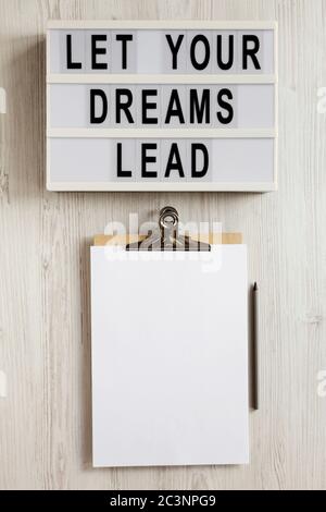 'Lass deine Träume führen' auf einem Leuchtkasten, Zwischenablage mit leerem Blatt Papier auf weißem Holzhintergrund, Draufsicht. Flach, über Kopf, von oben. Stockfoto